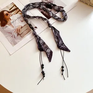 Dettaglio di una cintura a sciarpa in seta intrecciata con motivo paisley e perle nere