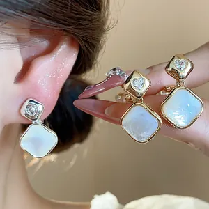 Close-up detail of 18k gold plated rhombus clip-on earrings with zircon and shell.