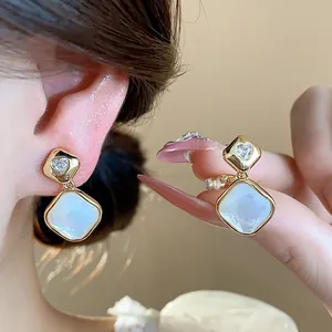 Close-up of 18k gold plated rhombus ear clips with zircon heart and white shell inlay