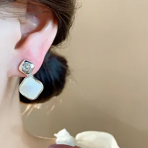 Close-up of 18k gold plated rhombus ear clips with zircon and white shell inlay.