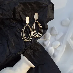 Close-up detail shot of matte gold geometric hollow earrings displayed on black paper.