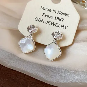 Close-up detail of 18k gold plated diamond-shaped clip-on earrings with white shell inlay