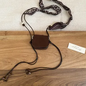 Dettaglio piatto di una cintura mini borsa in pelle marrone retrò con foulard di seta paisley