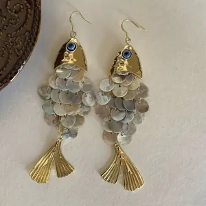 Gros plan sur des boucles d'oreilles poisson ethniques en nacre avec détail œil grec