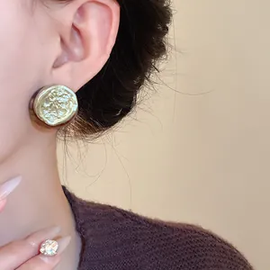 Detail macro view of a vintage gold-tone embossed floral stud earring worn by a model
