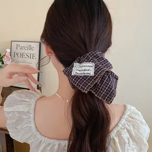 Κοντινή λεπτομέρεια καφέ καρό scrunchie μαλλιών με ετικέτα σε μακριά κυματιστά μαλλιά