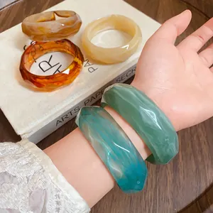 Detail shot of marbled acrylic faceted bangles in green and teal on a wrist.
