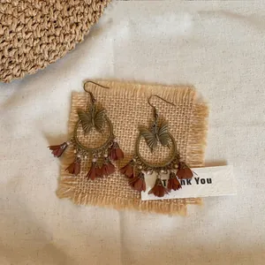 Vue détaillée des boucles d'oreilles créoles papillon en bronze avec pompons marrons