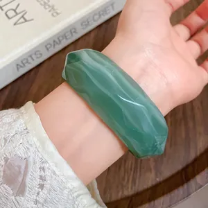 Macro view of a green marbled acrylic faceted bangle worn on a wrist with lace detail