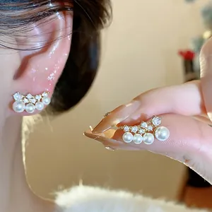 Close-up of elegant curved pearl and zircon stud earrings shown on ear and held by fingers