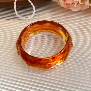 Macro detail of an amber marbled acrylic bangle with geometric faceted edges.