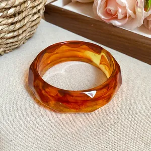 Close-up detail of a faceted amber acrylic bangle with elegant marbled pattern