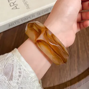 Detailed macro shot of a chunky amber marbled acrylic faceted bangle on a wrist