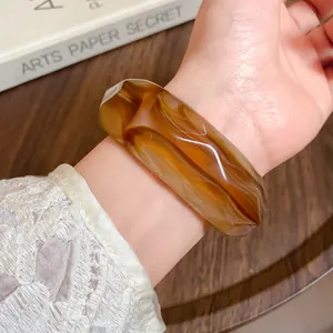 Detail shot of an amber marbled acrylic faceted bracelet on a wrist with lace.