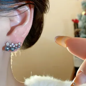 Close-up of 18k gold plated stud earrings with grey pearls and sparkling zircons on ear.