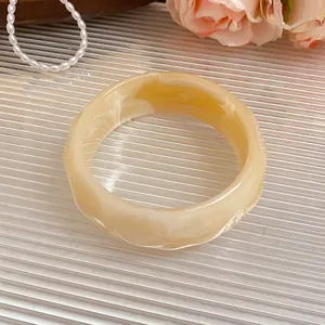 Detail view of a beige marbled acrylic bangle with faceted edges and striped patterns.