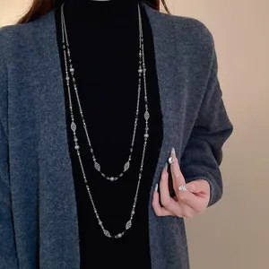 Nahaufnahme einer langen Retro-Perlen-Blumenkette auf Modell über einem grauen Cardigan-Oberteil.