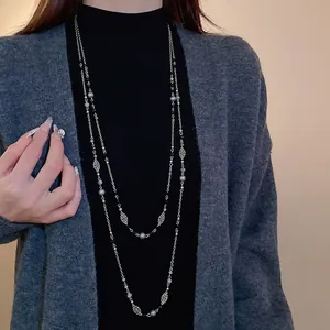 Lange Retro-Pulloverkette mit zarten Metallblumen und Kunstperlen auf schwarzem Top