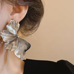 Detailed close-up of a large silver metal flower stud earring with textured petals