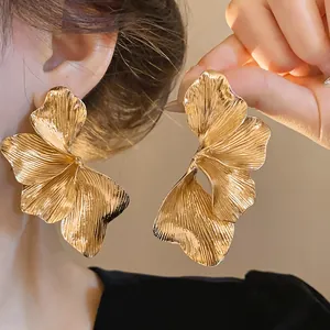 Detailed macro view of golden metallic ginkgo leaf earrings with pleated texture