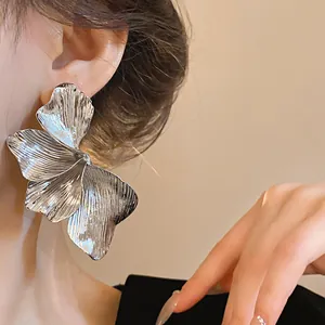 Detailed close-up of a large silver metallic flower stud earring with textured petals