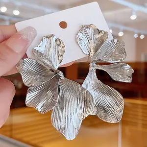 Detailed macro view of oversized silver flower petal earrings with realistic metal textures.