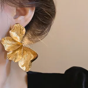 Elegant large golden metallic flower earring with brushed texture worn on a model's ear