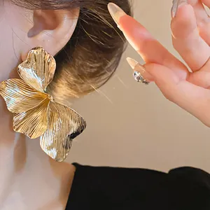 Detailed macro view of a large textured gold flower stud earring worn on an ear