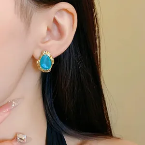 Nahaufnahme goldener Ohrringe im Vintage-Stil mit blauem Stein am Ohr des Models.