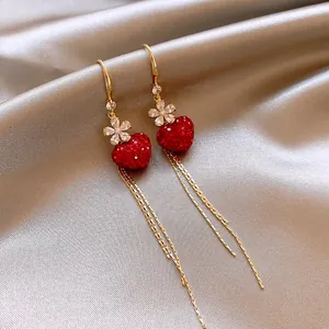 Dettaglio di orecchini a goccia in oro con cuore di cristallo rosso e eleganti fiori luccicanti.