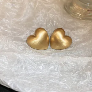 Primo piano dettagliato di orecchini a cuore in oro opaco su sfondo bianco strutturato.