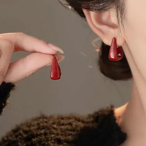 Detailed view of glossy red geometric hoop earrings worn by a model in soft lighting