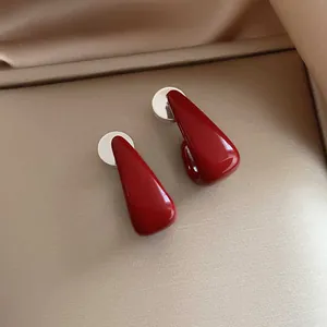 Detail view of minimalist red drip oil geometric stud earrings with silver posts.