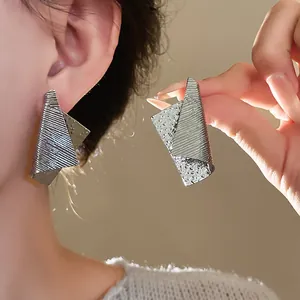 Detail view of irregular textured silver metal earrings on an Asian model's ear.