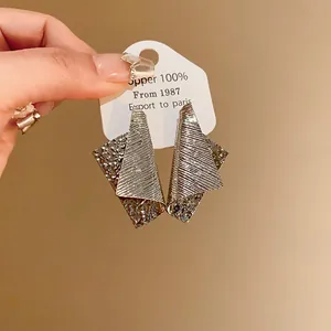 Close-up detail of irregular silver needle metal earrings with unique striped texture