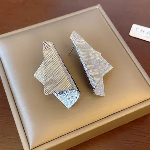 Detailed macro view of silver irregular geometric earrings with striped and hammered textures.