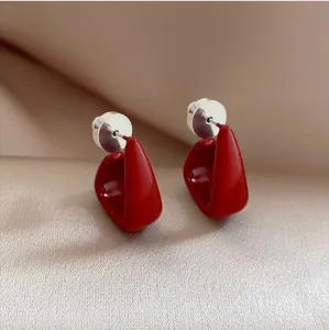 Close-up of glossy red geometric enamel earrings on a soft silk background for women.
