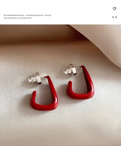 Detailed close-up of red enamel geometric stud earrings on a silky cream fabric