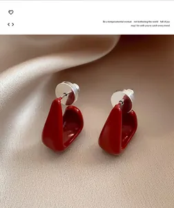 Detailed close-up of red enamel geometric stud earrings on luxury champagne silk background