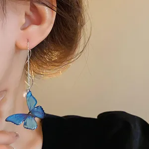 Close-up view of elegant blue butterfly pearl earrings on model showing detail