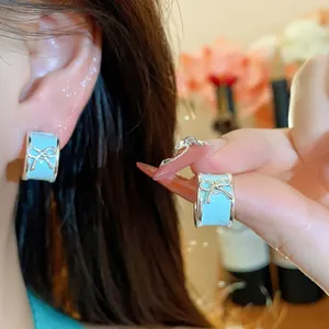 Close-up of light blue enamel bow C-shaped stud earrings shown on ear and held by hand.