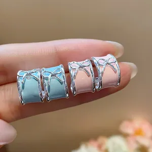 Close-up of stylish pastel pink and blue enamel bow C-shape earrings held on fingers