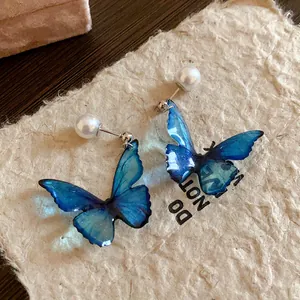 Detailed view of elegant blue gradient butterfly earrings with pearls on rustic paper
