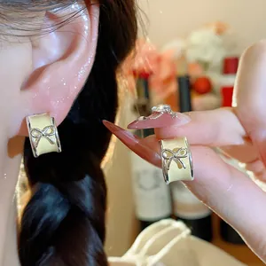 Close-up detail of stylish pale yellow enamel C-shaped bow stud earrings worn on ear