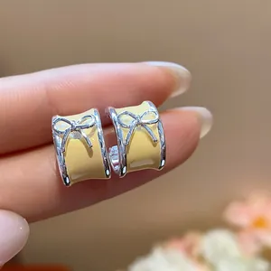 Close-up detail of yellow enamel C-shaped stud earrings with a delicate silver bow.