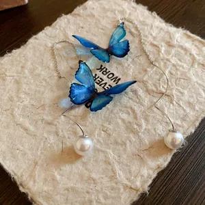 Detail view of blue butterfly pearl earrings on textured handmade paper background