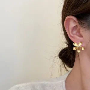 Close-up of minimalist matte gold flower stud earrings worn by a model for a chic look