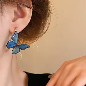 Detailed close-up showing an elegant blue butterfly wing drop earring on model's ear