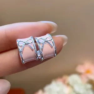 Detail close-up of pink enamel C-shaped hoop earrings featuring a silver bow design.
