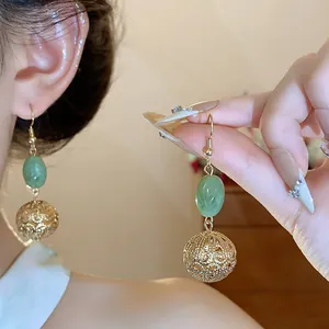 Detailed view of vintage resin earrings with gold hollow ball pendant on ear and hand
